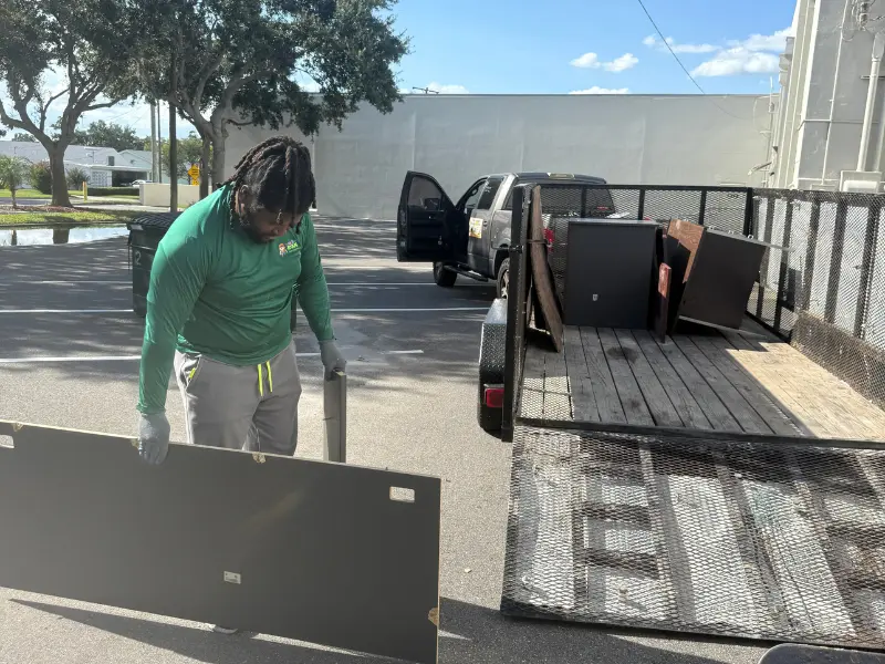 Dibs On Your Junk crew member in branded green shirt loading a large furniture panel onto a junk removal trailer in Mulberry, FL